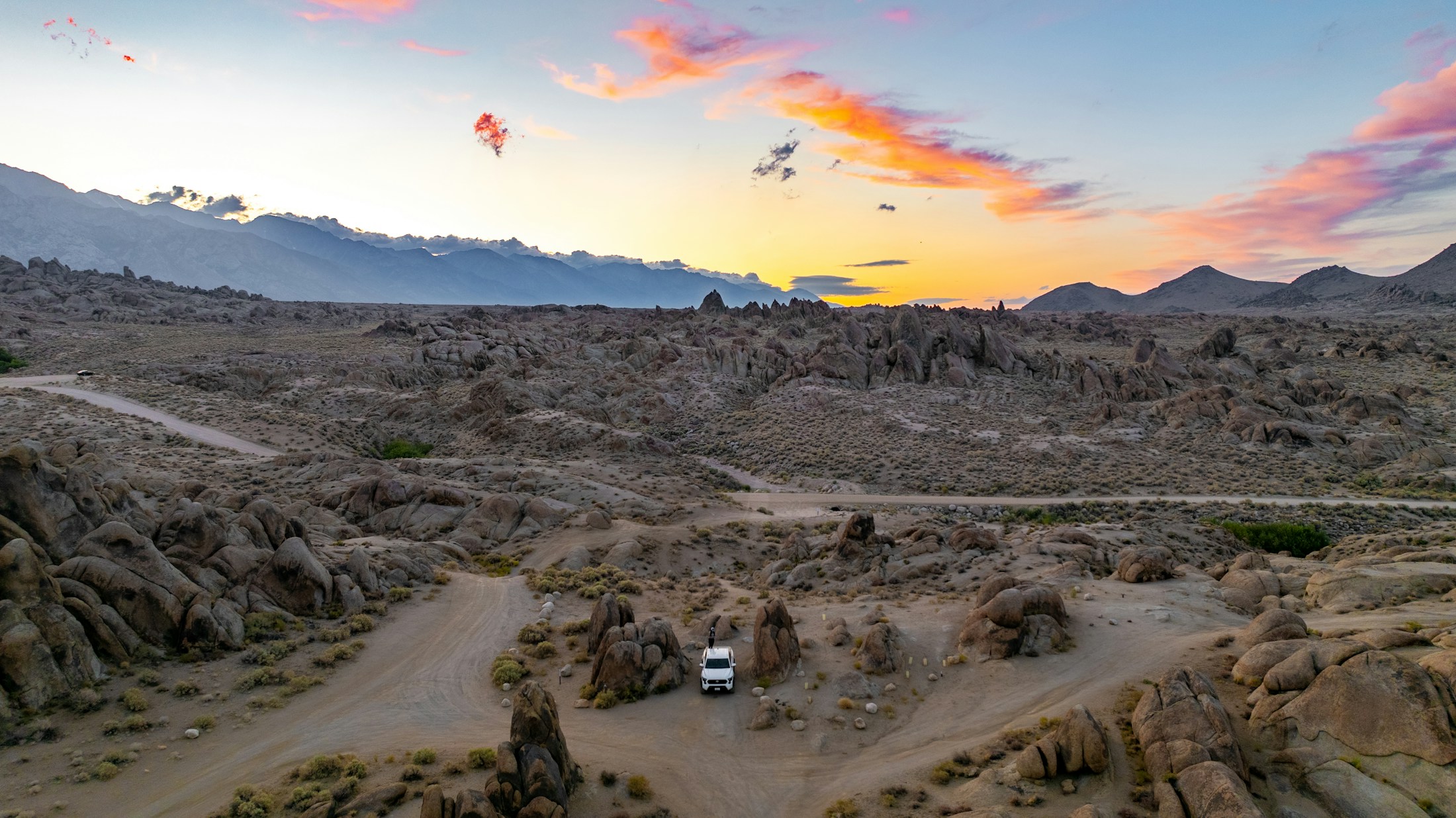 Camping vehicle amid broad desert hills at sunset